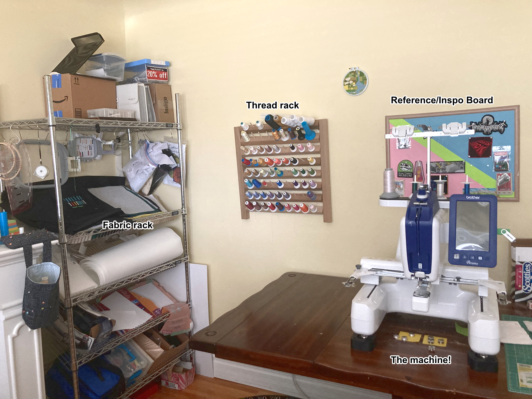 A photograph showing more of the embroidery workspace. The embroidery machine, thread rack, and fabric rack are pictured.